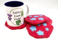 two red and blue coasters next to a coffee mug with the words amber goes violet on it