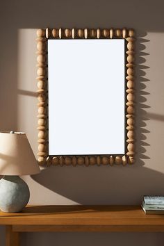 a table with a lamp and a mirror on it next to a wall mounted wooden bead frame