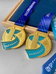 two gold and blue medals sitting on top of a wooden box next to each other