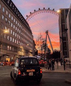 a black car driving down a street next to tall buildings with a ferris wheel in the background