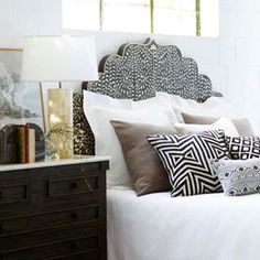 a bed with white sheets and black and white pillows on it's headboard