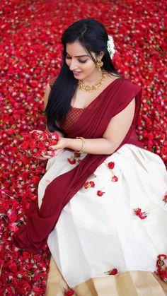 a woman in a red and white sari sitting on the ground with flowers around her