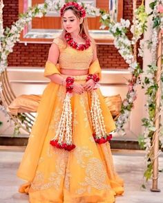 a woman in a yellow and red wedding dress with flowers on her head, standing next to a flower arch