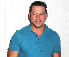 a man in a blue shirt is holding a piece of pizza and posing for the camera