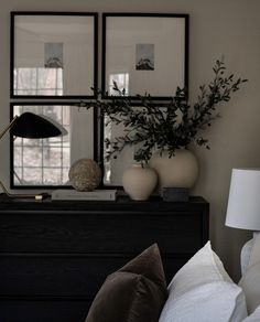 a black dresser topped with two vases filled with flowers and greenery next to a mirror