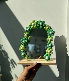 a person holding up a green and white wreath made out of beads on a shelf