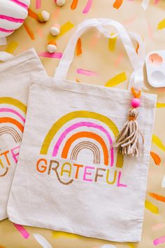 two bags with the words grateful and a rainbow painted on them sitting next to confetti