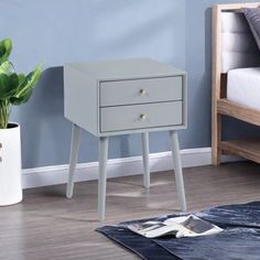 a white nightstand with two drawers next to a bed and potted plant on the floor