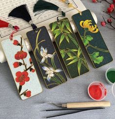 four bookmarks with flowers painted on them next to paint brushes and paints in bowls