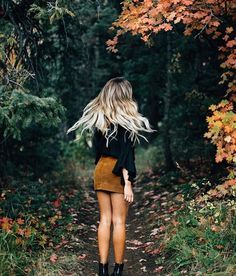 a girl walking down a path in the woods with her hair blowing back and looking at trees