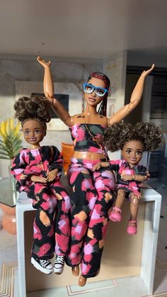 two dolls sitting on top of each other in matching outfits, one is wearing sunglasses and the other has her arms up