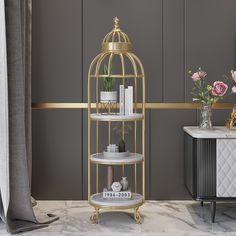 a gold birdcage filled with books and flowers on a marble floor next to a mirror