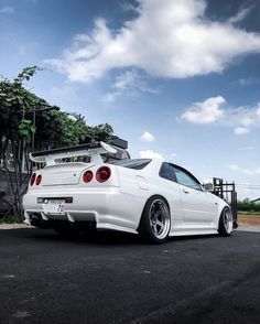 the rear end of a white car parked on top of a parking lot next to trees