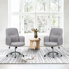 two gray chairs sitting on top of a rug in front of a white wall and window