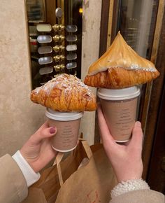 two people holding up coffee cups with pastries on them