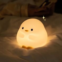 a little light that looks like a penguin on a bed with white sheets and pillows