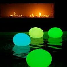 three glowing balls sitting in front of an open fire place with the reflection of it on the water