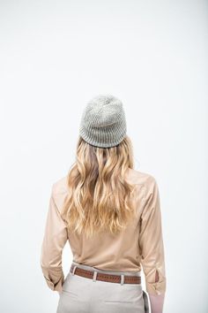 a woman with long blonde hair is wearing a hat and beige shirt while standing in front of a white wall