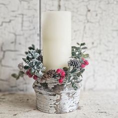 a white candle sitting on top of a wooden container filled with holly and pine cones