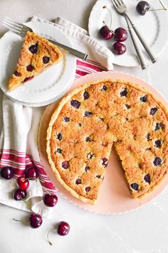 a piece of pie on a plate next to a fork, knife and cherries