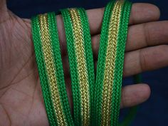 a hand holding two green and gold braided bracelets