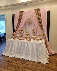 a table topped with lots of cakes and cupcakes next to a pink drape