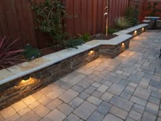 an outdoor patio with stone walls and lights on the side walk, next to a wooden fence