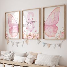 two pink butterfly prints hanging on the wall above a bench with pillows and pillow cases