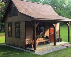 a small wooden cabin with a porch and covered patio area in the grass, surrounded by trees