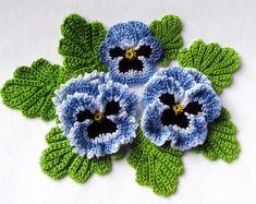 three crocheted blue flowers with green leaves