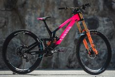 a pink and black mountain bike parked in front of a rock wall