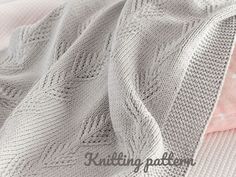 a white knitted blanket laying on top of a pink and white bed coverlet