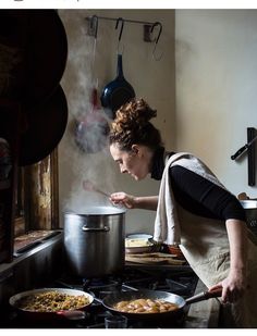 a woman in an apron is cooking on the stove with a pot and pan next to her