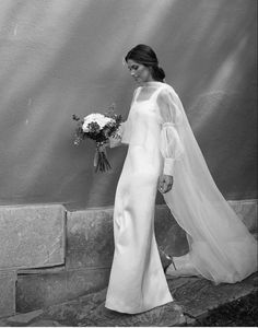 black and white photograph of woman in wedding dress walking up steps with bouquet on hand