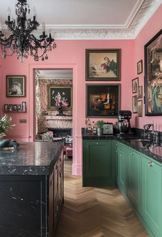 a pink kitchen with green cabinets and black counter tops is pictured in this image, the walls have pictures on them