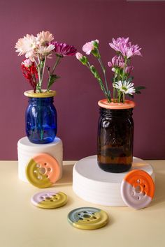 three vases with flowers in them sitting on a table next to buttons and buttons