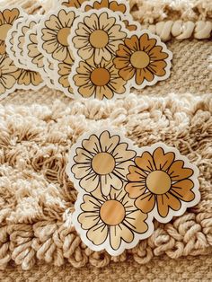 three stickers with flowers on them are sitting on a blanket in front of a pile of crocheted material