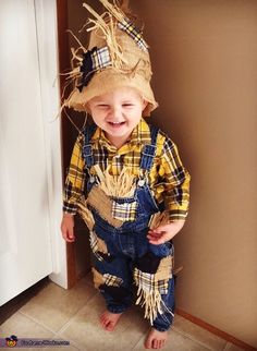 a little boy wearing overalls and a scarecrow hat standing in front of a door