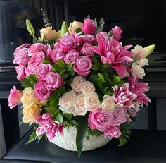 a bouquet of pink and yellow flowers in a white basket on a black table next to a piano