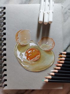 some colored pencils are next to a drawing of an egg and two eggs on a plate