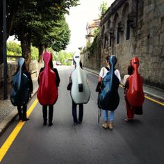 four people are walking down the street with guitars on their backs