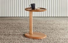 a wooden table with a cup on it in front of a white wall and carpet