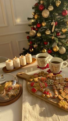 a christmas tree is in the background with cookies on a tray and two mugs