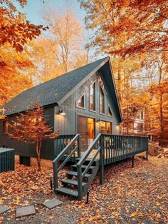 a small cabin in the woods surrounded by trees with leaves on the ground and stairs leading up to it