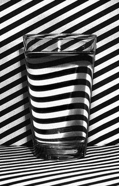 a black and white photo of a glass with water in it on a striped surface