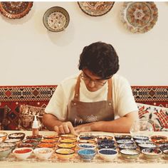 a man in an apron working on some food at a table with bowls and plates