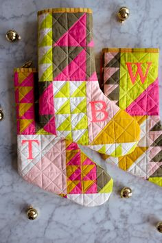 two oven mitts and one pot holder on a marble countertop with gold bells