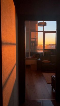 an open door leading to a living room with the sun setting in the window behind it