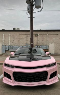 a pink sports car parked in a parking lot next to a pole with an antenna on it