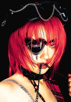 a woman with red hair and black eye makeup is wearing a chain around her neck